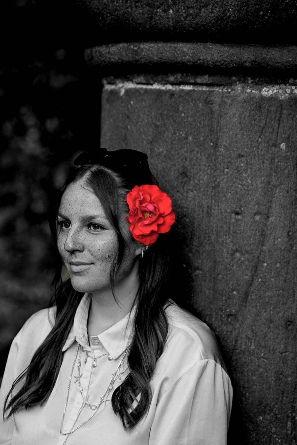 Schwarz-Weiß-Porträt einer jungen Frau mit roter Rose im Haar