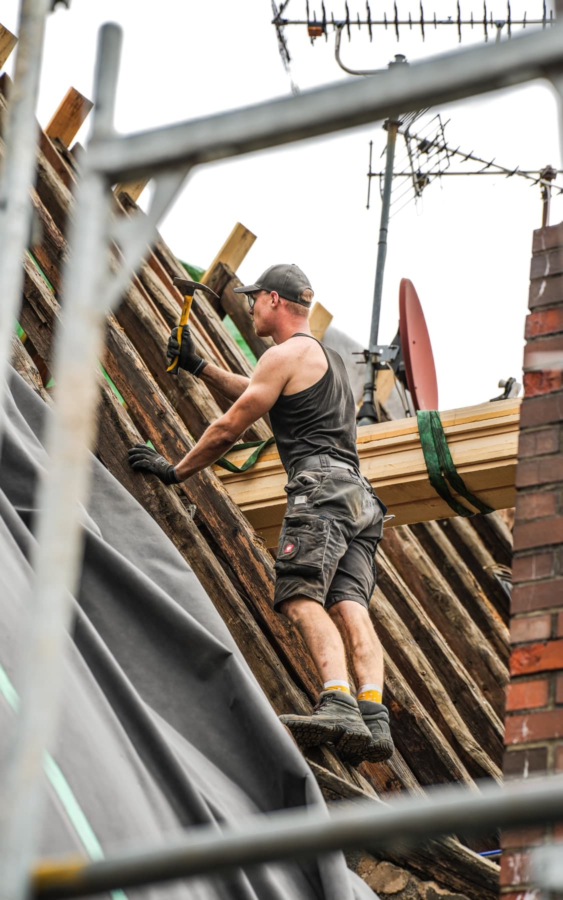 Dachdecker schlägt auf einem Gerüst am freigelegten Dachstuhl einen Nagel ein